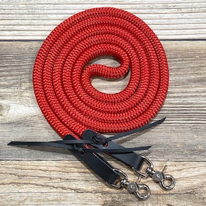 May include: A coiled red rope with black leather straps and silver-coloured metal clasps. The rope is thick and appears to be made of a durable, woven material. The leather straps are attached to the rope and have metal clasps for easy attachment. Equestrian equipment.