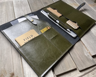May include: A green leather portfolio with multiple pockets and compartments. The portfolio is open and contains a notebook, a pen, a phone, and a credit card. The text "FIELD NOTES" is visible on the notebook.
