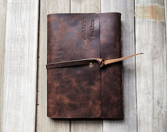 May include: A brown leather photo album with a leather strap and a brass buckle. The album is engraved with the text "Alexa & Chris  Scrapbook".