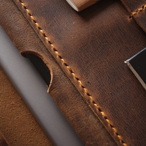May include: Close-up of a brown leather travel wallet with a stitched edge and a black passport holder with the word "PASSE" visible.