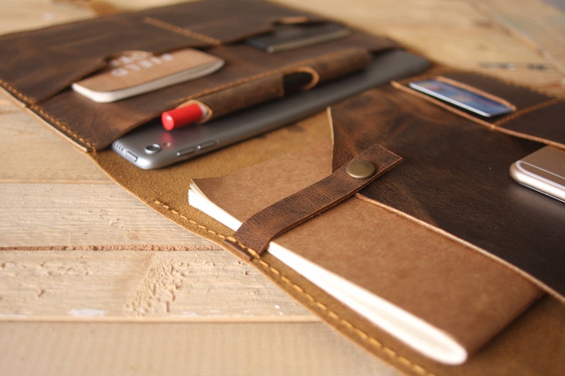 May include: A brown leather portfolio with multiple pockets and compartments. The portfolio is open and shows a tablet, a notebook, a pen, and a credit card.