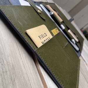 May include: A green leather portfolio with multiple pockets and a small notebook that says "FIELD NOTES" on the cover.