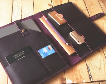 May include: A dark purple leather portfolio with multiple pockets and compartments. The portfolio is open and contains a tablet, a notebook, a pen, a credit card, a passport, and a phone.