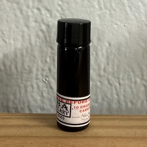 Può includere: Un piccolo flacone di vetro nero con un tappo nero. Il flacone ha un'etichetta bianca con il testo "The Apothecary" e "10 gocce di olio vettore".