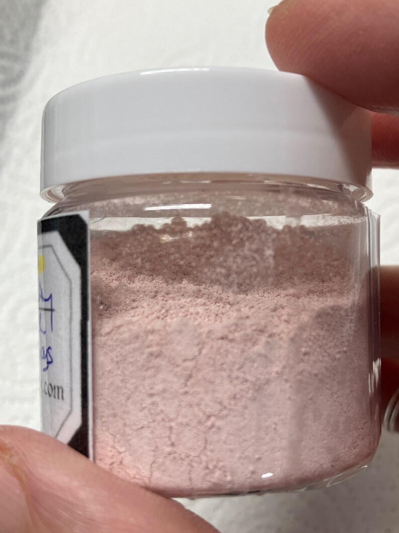 Pu&ograve; includere: Un piccolo barattolo di vetro trasparente con un coperchio bianco riempito di polvere rosa chiaro. Il barattolo ha un'etichetta con il testo "Sugar & Spice" e un indirizzo di sito web.