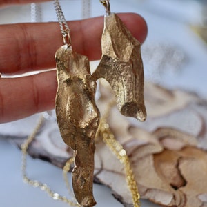May include: Two gold-toned necklaces with abstract, textured pendants. The pendants are shaped like leaves or wings and have a rough, organic look.