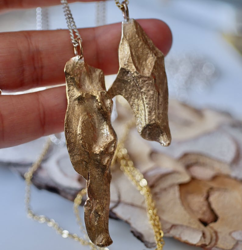May include: Two gold-toned necklaces with abstract, textured pendants. The pendants are shaped like leaves or wings and have a rough, organic look.