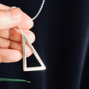 May include: A silver triangle pendant necklace with a delicate chain. The triangle is hollow and has a simple, modern design.