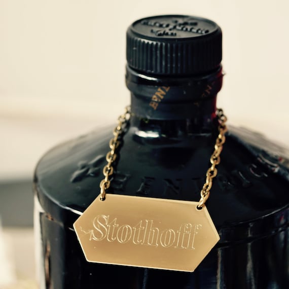 A hand-engraved brass tag that hangs around a decanter's neck with a custom label — turns any bottle into a personalized bar piece with old-world apothecary charm.
