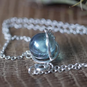 May include: A silver chain necklace with a blue glass orb pendant. The orb is encased in a silver wire frame.