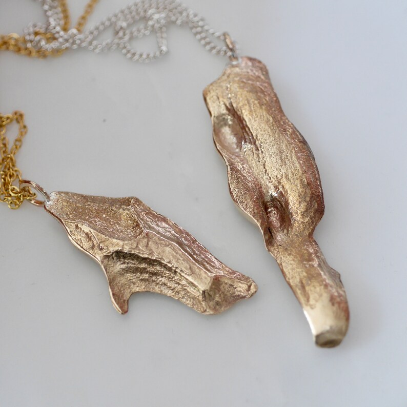 May include: Two gold-toned pendants shaped like pieces of driftwood, hanging from a silver chain.