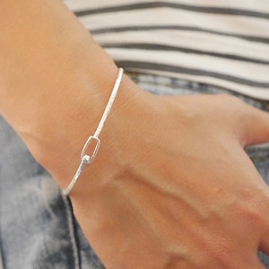 Może przedstawiać: Srebrna bransoletka typu bangle z fakturowanym wykończeniem i małym prostokątnym zapięciem.
