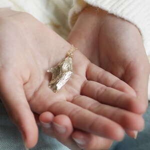 May include: A gold necklace with a unique, textured pendant shaped like a leaf. The pendant has a rough, organic texture and a slightly irregular shape.