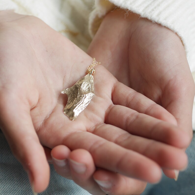 May include: A gold necklace with a unique, textured pendant shaped like a leaf. The pendant has a rough, organic texture and a slightly irregular shape.