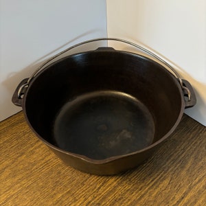May include: A black cast iron pot with a single wire handle. The pot is empty and has a worn, rustic look.