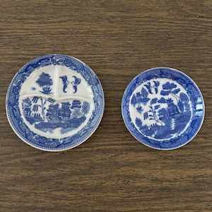 May include: Two blue and white porcelain plates with a willow pattern design. The larger plate is divided into three sections.