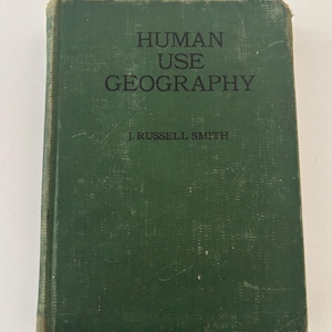May include: A vintage hardcover book titled "HUMAN USE GEOGRAPHY" by J. Russell Smith. The book has a dark green cover with the title and author's name in black lettering. The book's cover shows signs of wear.