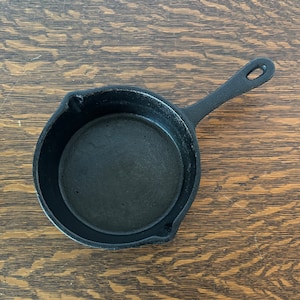 May include: A small black cast iron skillet with a single handle. The skillet is empty and has a smooth, black interior.