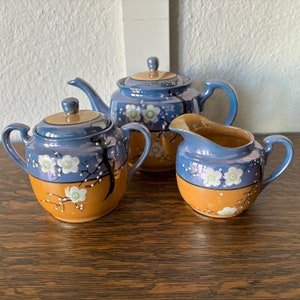 May include: A blue and brown tea set with a floral design. The set includes a teapot, creamer, and sugar bowl.