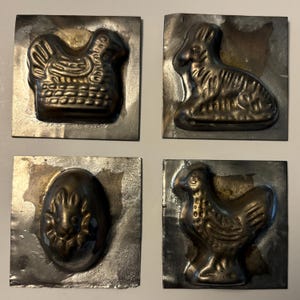 May include: Four vintage metal molds for making chocolate Easter treats. The molds feature a chicken, a rabbit, an egg, and a chicken.