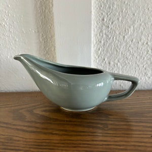 May include: A light gray ceramic gravy boat with a handle. The boat has a smooth, glossy finish.