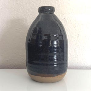 May include: A dark blue ceramic vase with a rounded body and a narrow neck. The vase has a glossy finish and a textured surface. The base of the vase is a light brown color. The vase is approximately 8 inches tall.