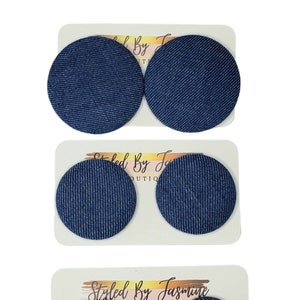 Puede incluir: Tres pares de pendientes de tela vaquera. Cada par es de un tamaño diferente. Los pendientes son redondos y tienen una tela vaquera azul con costuras blancas. Los pendientes están en una tarjeta blanca con el texto "Styled By Jasmine Boutique".