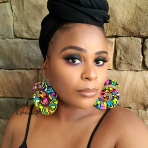May include: A person wearing a black headscarf and a black tank top with large colorful spiral earrings. The earrings are made of fabric and have a geometric pattern.