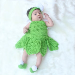 May include: A baby wearing a green crocheted fairy costume with white pom-poms on the hat and shoes.