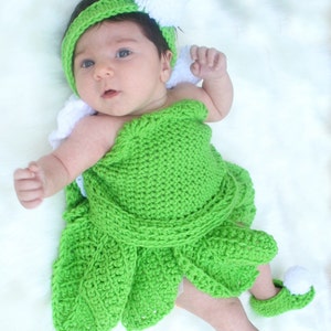 May include: A baby wearing a green crocheted dress with white pom-poms on the hat and shoes.