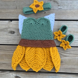 May include: A crocheted sunflower costume for a baby, featuring a green bodice, brown and yellow skirt, and matching sunflower headband and booties.