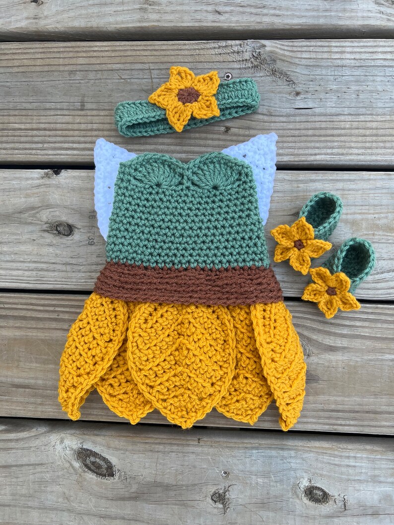 May include: A crocheted sunflower costume for a baby, featuring a green bodice, brown and yellow skirt, and matching sunflower headband and booties.