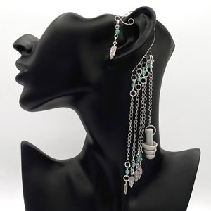 May include: Silver ear cuff with a dangling chain featuring turquoise beads and small silver charms. The chain is attached to the ear cuff with a small silver ring.