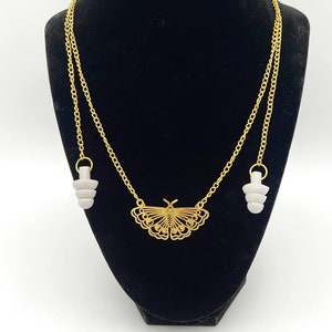 May include: A gold chain necklace with a butterfly pendant and two white earplugs attached to the ends. The necklace is displayed on a black velvet mannequin.