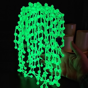 May include: A long strand of glow-in-the-dark green beads connected by thin rods, forming a cascading, organic shape.