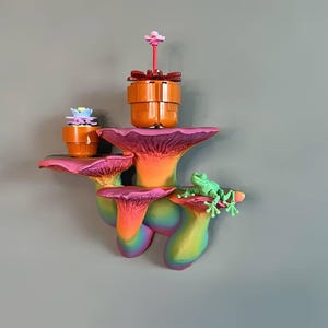 Puede incluir: Un conjunto de tres estantes de pared en forma de hongo de colores arcoíris con una pequeña planta en maceta y una figurita de rana verde en la parte superior.