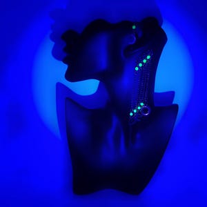 May include: A black mannequin bust with a silver chain necklace with green accents. The necklace is on display against a blue background.