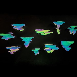 Può includere: Una collezione di sculture astratte a forma di nuvola, nei toni del blu, verde e viola, su sfondo nero. Le sculture hanno un aspetto luminoso, simile al neon, che suggerisce un tema fantasy o fantascientifico.