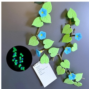 May include: Decorative vine magnets with blue flower accents and green leaves. A small notepad is attached with a grocery list. A separate black circle shows glowing vine and flower magnets.