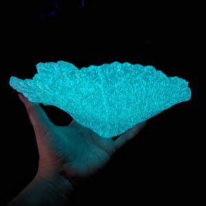 Puede incluir: Una mano sosteniendo una gran escultura de resina de color azul verdoso, que brilla y se asemeja a un coral o una anémona de mar.