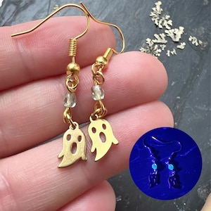 以下が含まれることがあります： ぶら下がりデザインのゴールドカラーのゴーストイヤリング。各イヤリングは、ビーズのチェーンとゴールドトーンのイヤーフックから吊り下げられた小さな切り抜きゴーストチャームが特徴です。イヤリングはピアス用に設計されており、ハロウィーンに適しています。