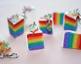 Könnte beinhalten: Ein Set mit sieben Regenbogen-Kuchenstück-Anhängern mit weißem Zuckerguss und bunten Streuseln. Jeder Anhänger hat einen silbernen Schlüsselring.