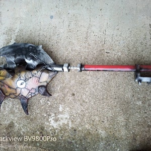 Puede incluir: Un arma de estilo fantástico de metal pintada a mano con un mango rojo, una cadena y un extremo con púas. El arma tiene un diseño detallado, texturizado y multicolor.