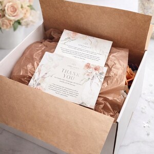Puede incluir: Una caja de env&iacute;o de cart&oacute;n blanco abierta, forrada con papel de seda marr&oacute;n, que contiene dos tarjetas rectangulares con ilustraciones florales. La tarjeta superior dice Thank You y Aisle and Ivy Studio, con m&aacute;s texto.