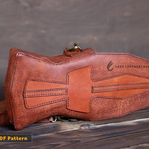 May include: A brown leather crossbody bag with a unique geometric design and stitching. The bag has a flap closure and a metal buckle. The bag is made by Lexy Leathercraft.