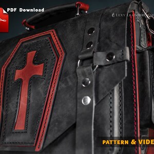 Puede incluir: Bolso de cuero negro con una cruz roja en la parte delantera. El bolso tiene detalles de costura roja y una hebilla plateada. El bolso est&aacute; etiquetado como "PATTERN & VIDEO".