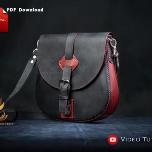 Op de afbeelding: Zwarte leren zadeltas met rode accenten en een gespsluiting. De tas heeft een lange, verstelbare riem en een klepsluiting. De woorden "PDF Download" en "Video Tutorial" zijn zichtbaar.