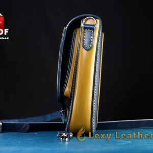 May include: A yellow leather crossbody bag with a blue leather trim and a silver metal buckle. The bag has a strap that is attached to the bag with a silver metal ring.