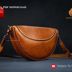Könnte beinhalten: Braune Ledersatteltasche mit geschwungenem Design und verstellbarem Riemen. Die Tasche hat weiße Nähte und goldfarbene Beschläge. Das Bild enthält den Text "PDF DOWNLOAD" und "VIDEO TUTORIAL".