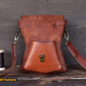 May include: A brown leather crossbody bag with a flap closure and a small front pocket. The bag has a brass buckle and a strap with a metal clasp. The bag is on a wooden surface.  PDF Pattern.